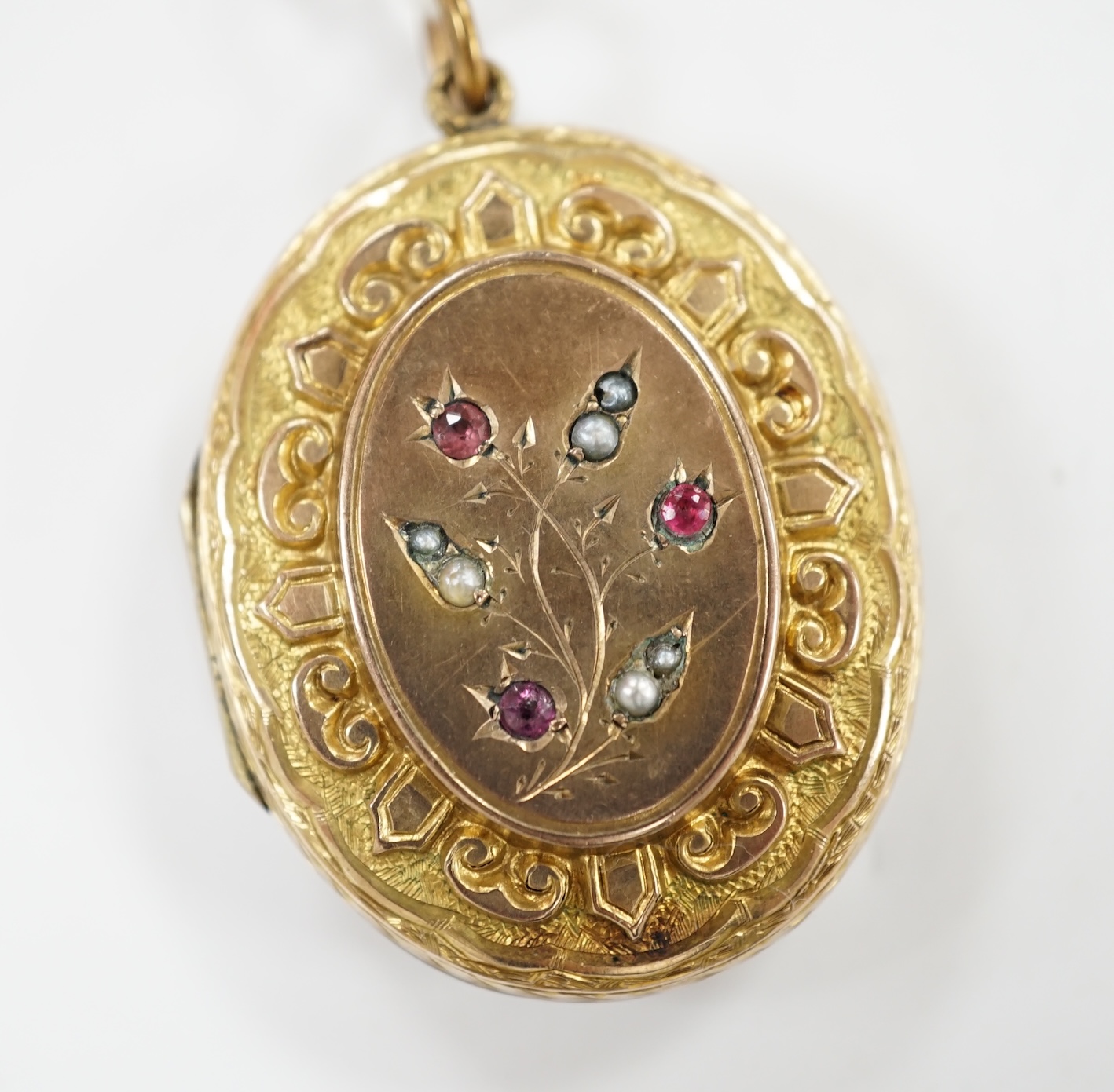 A Victorian engraved yellow metal overlaid, garnet and seed pearl set oval locket, 37mm. Condition - fair